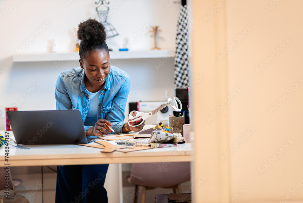 Female fashion tailor working on dress design in her workshop using laptop. Female fashion tailor working on dress design in her workshop using laptop.