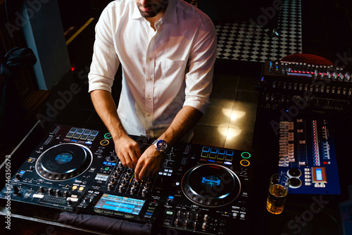 Crop DJ plays live set and mixing music on turntable console in the night club. Disc Jokey Hands on a sound mixer station at club party. DJ mixer controller panel for playing music and partying.