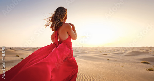 Desert adventure. Young arabian Woman in red silk dress in sands dunes of UAE desert at sunset, fantastic view. The Dubai Desert Conservation Reserve, United Arab Emirates.