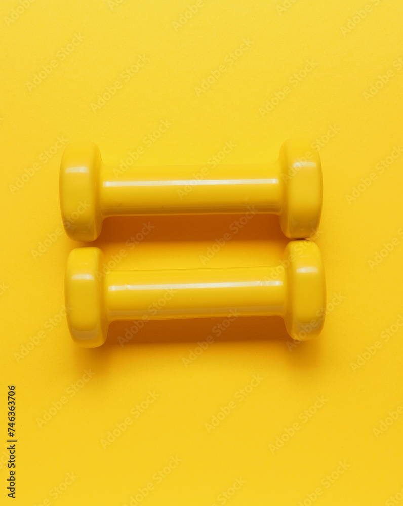 Two yellow dumbbells on a yellow background Two yellow dumbbells on a yellow background