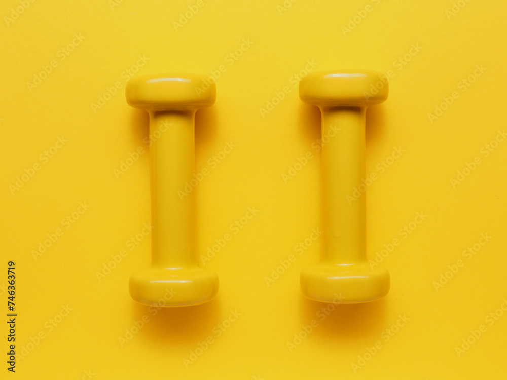 Two yellow dumbbells on a yellow background Two yellow dumbbells on a yellow background
