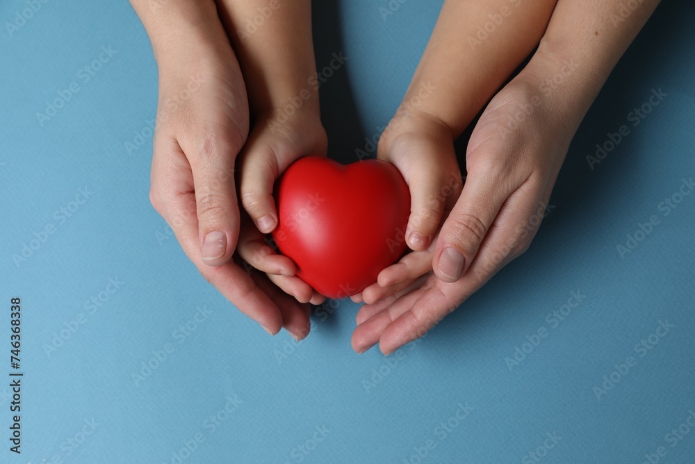 Obraz premium Mother and her child holding red decorative heart on light blue background, top view