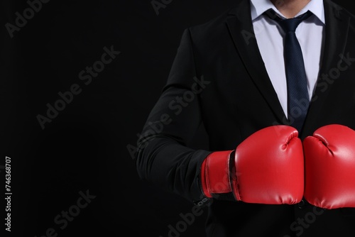 Businessman in suit wearing boxing gloves on black background, closeup. Space for text © New Africa