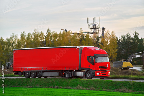 A red truck transports a cargo truck travels through a scenic route bathed in sunset. freight truck embarks on its journey under the warm gaze of the evening sun. Global shipping and logistics chain.