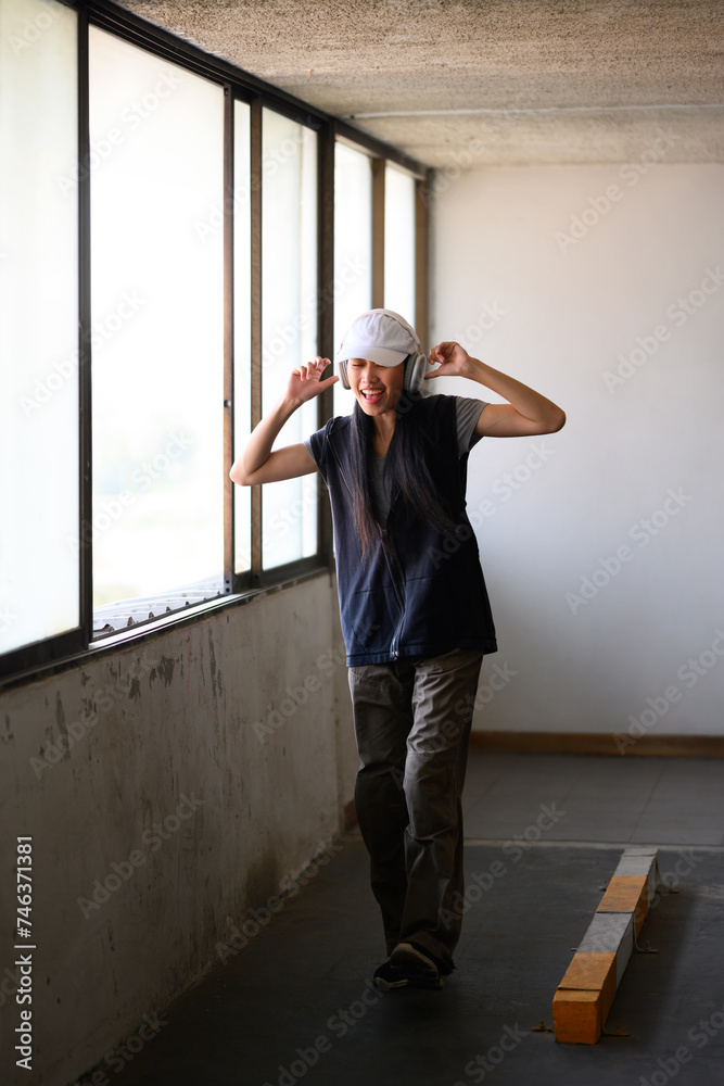 Happy female dancer wearing headphone and street clothes dancing in parking garage