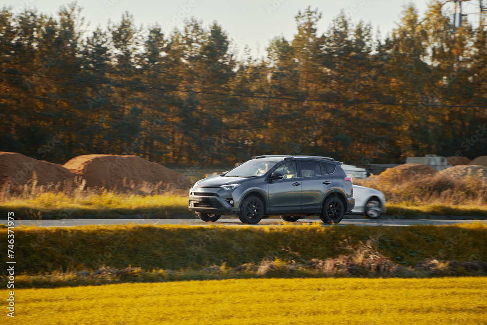 A hybrid SUV car journeys along a scenic road with majestic nature and a golden sunset in the backdrop.