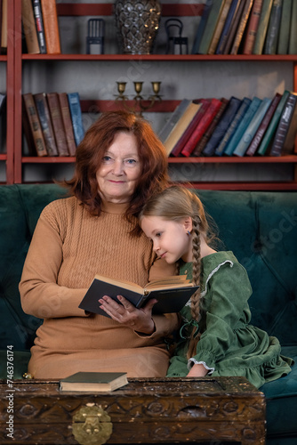 Happy grandma and granddaughter reading book together and having fun at home