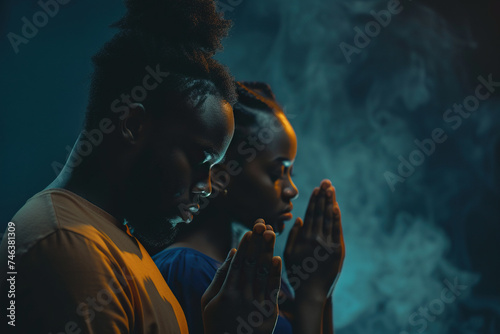 African American man and woman prays to god together on dark studio background. Cinematic effect