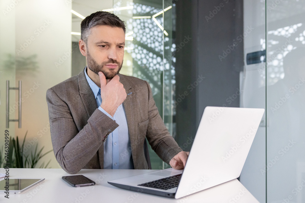 Thoughtful business professional analyzing data on laptop in modern office setting Thoughtful business professional analyzing data on laptop in modern office setting