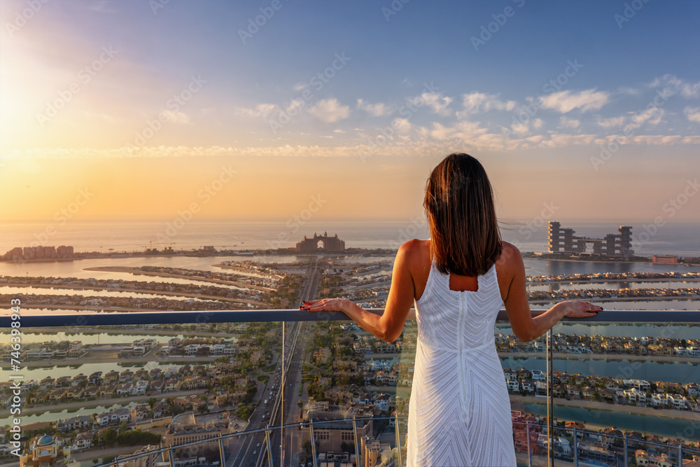 A beautiful woman in a white dress enjoys the sunset view over the Palm in Dubai, UAE