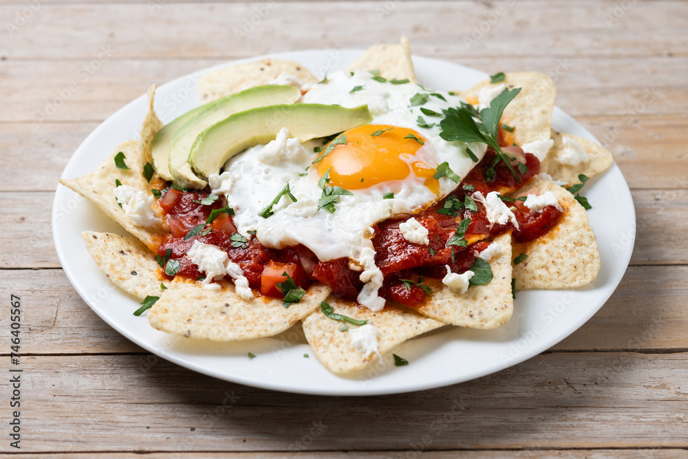 Traditional Mexican breakfast red chilaquiles with egg on wooden table