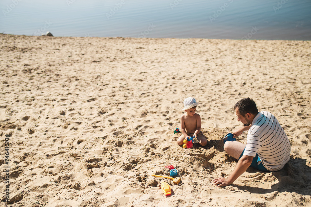 Father and 3 years son on beach building sand castle with plastic toys . single father solo parent. Involved parenting. Relaxing and playing outdoors with family Father and 3 years son on beach building sand castle with plastic toys . single father solo parent. Involved parenting. Relaxing and playing outdoors with family