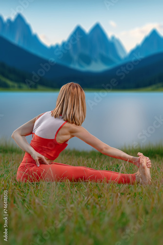 Relaxed young yoga woman stretching body near lake in mountains, Perfect symmetry: Young woman's yoga pose aligns with the beauty of a mountain lake © Denys Kurbatov