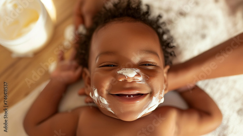 A young black mother moisturizes her baby with baby cream. Mother and child, child care, close-up portrait of a dark-skinned baby, smiling child. Bokeh in the background. photo