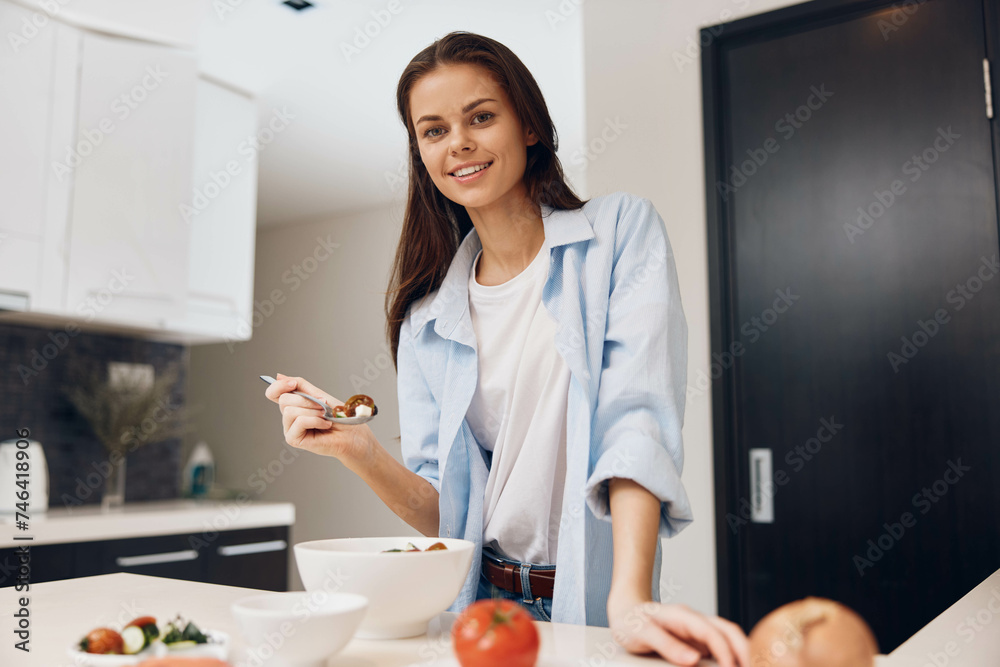 Woman cooking healthy vegetable meal in kitchen with bowl of vegetables and spoon in hand Woman cooking healthy vegetable meal in kitchen with bowl of vegetables and spoon in hand