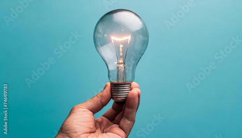 Male hand holds a light bulb isolated on blue background. Concept of idea, ingenuity and creativity