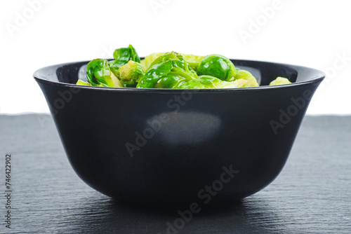 Cooked organic brussels sprouts in black bowl isolated on white background.