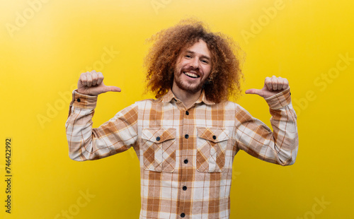 Smiling man showing thumbs down gesture in front of yellow wall photo