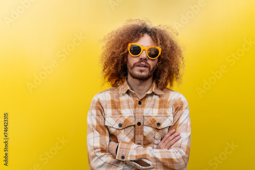 Man wearing sunglasses and standing with arms crossed in front of yellow wall photo