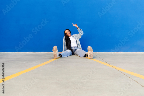 Happy woman showing peace sign in front of blue wall photo