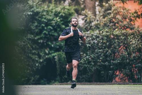 Determined young man running outside in the park. Fit boy doing exercise outdoor. Beautiful sporty male run alone. Sweaty athlete training with towel. Wellness, health, sport, fitness open air concept © Fabio Principe