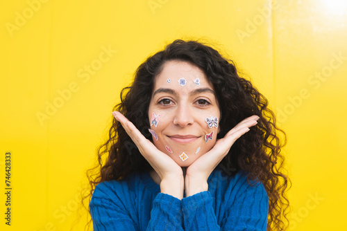 Curly haired woman with stickers on face against yellow background photo