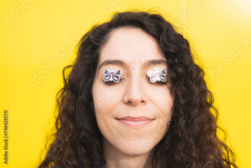 Smiling curly haired woman with butterfly stickers on eyes against yellow background photo
