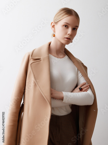 Portrait of young beautiful girl wearing stylish oversize coat isolated over white background. Concept of beauty, fashion, human emotions. Model looks composed and sexy