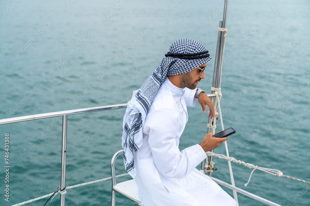 Arab businessman speaking on mobile phone working corporate business during travel on private catamaran boat yacht sailing in the ocean. Arabic man enjoy luxury outdoor lifestyle on summer vacation.