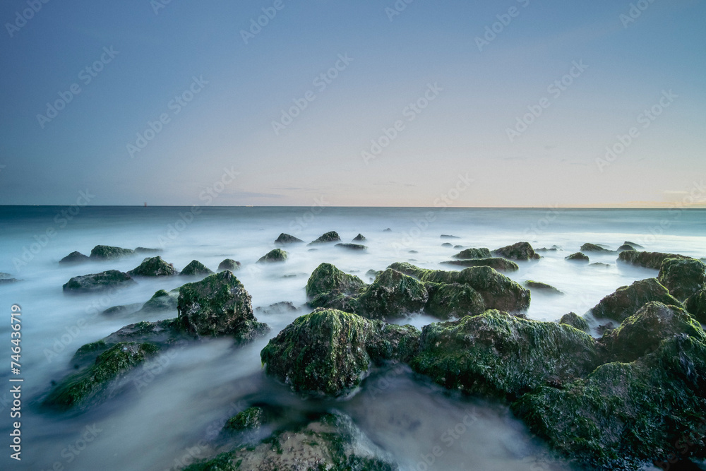 Bollards along the coast with green seaweed and evening sky during sunset. long exposure seascape with milky waves
