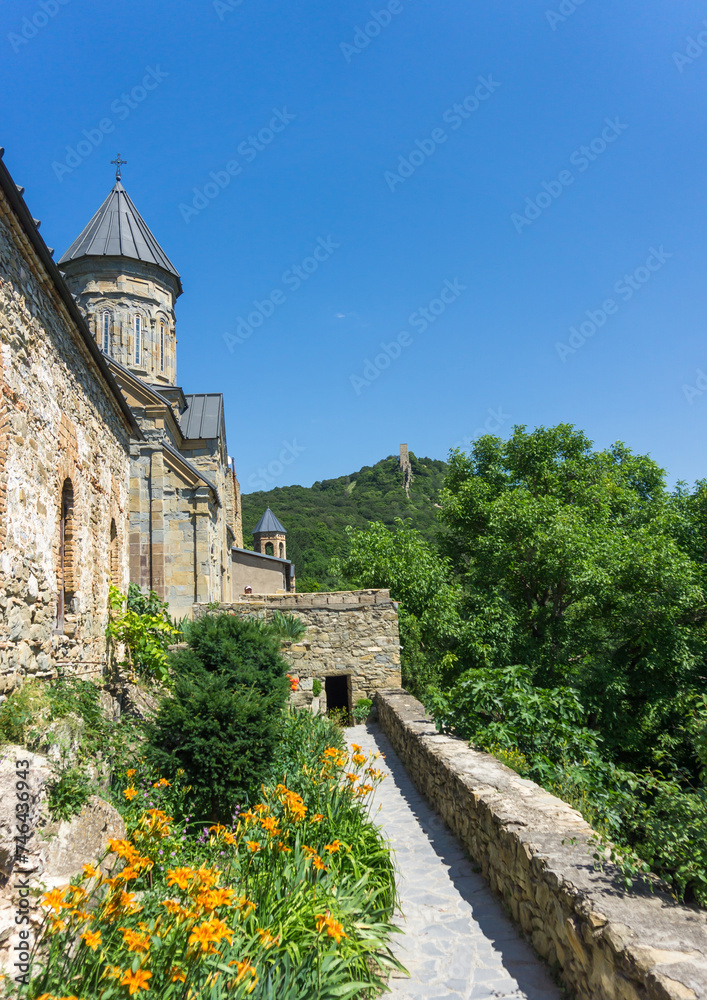 Inner courtyard of the monastery. Stone wall and dome of church, trees and flowers. Tower on the hill.
