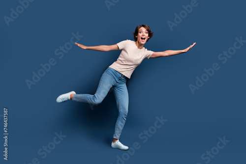 Full size photo of attractive young woman flying have fun spread hands dressed stylish white clothes isolated on dark blue color background