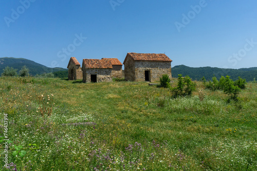 Three small churches on the territory of a medieval fortress. Green field with flowers. Mountains and bright blue sky in the background.