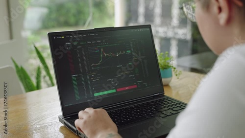 Focused individual monitors market charts on laptop in sunlit office. Analyzing real-time trading data, considering investment strategies. Professional trader engaged in day trading, clicking mouse.