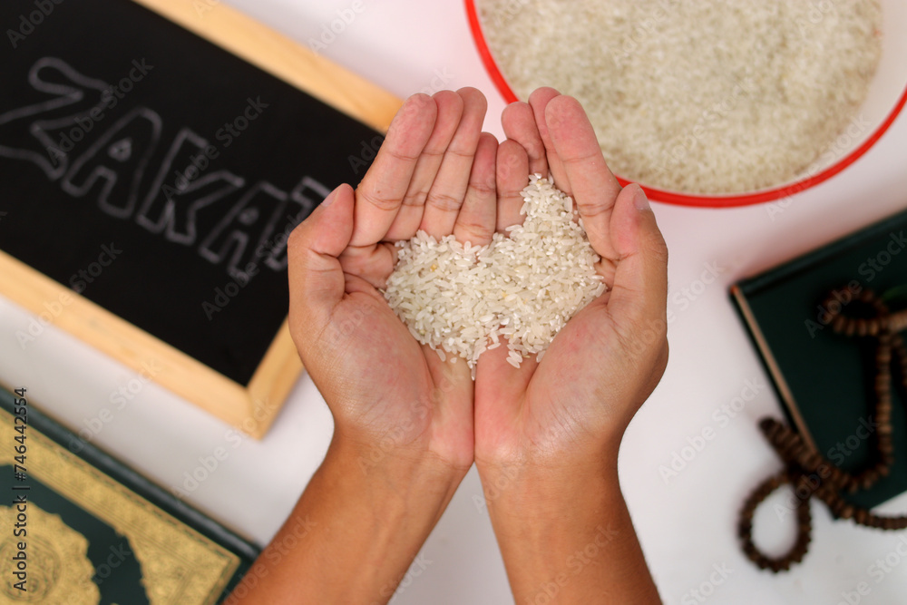 Hand holding a pile of rice for Zakat al-Fitr, with the Holy Quran ...