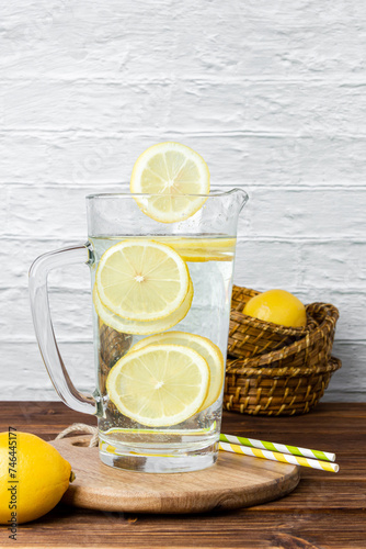Water with lemons in jug on a cutting board on a wooden table.