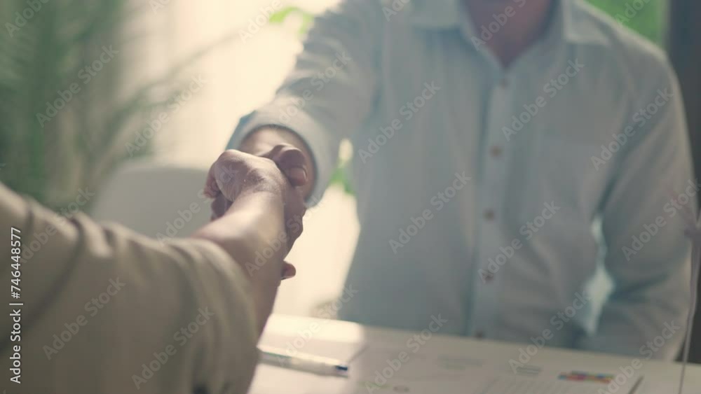 Two professionals seal a deal with a handshake over a table covered with sustainability reports and business analysis documents. Two professionals seal a deal with a handshake over a table covered with sustainability reports and business analysis documents.