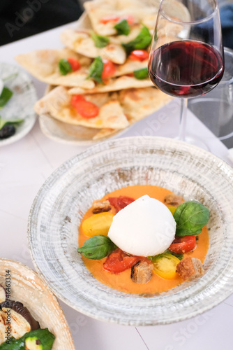 Mozzarella di buffalo on a plate with cherry tomatoes, tomato sauce, basil leaves, a glass of red wine, focaccia 