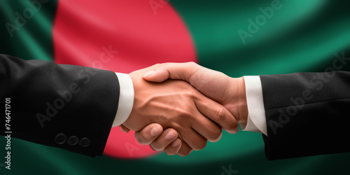 Businessman, diplomat in suits clasp hands for handshake over Bangladesh flag, agree on united success in trade, diplomacy, cooperation, negotiation, teamwork in commerce, gesture of greeting