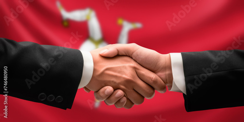 Businessman, diplomat in suits clasp hands for handshake over Isle of Man flag, agree on united success in trade, diplomacy, cooperation, negotiation, teamwork in commerce, gesture of greeting photo