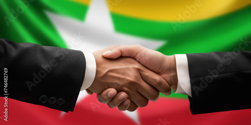 Businessman, diplomat in suits clasp hands for handshake over Myanmar flag, agree on united success in trade, diplomacy, cooperation, negotiation, support, teamwork in commerce, gesture of greeting