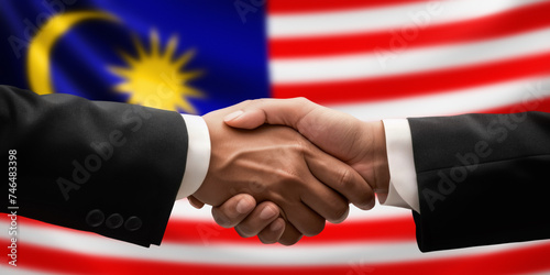 Businessman, diplomat in suits clasp hands for handshake over Malaysia flag, agree on united success in trade, diplomacy, cooperation, negotiation, support, teamwork in commerce, gesture of greeting