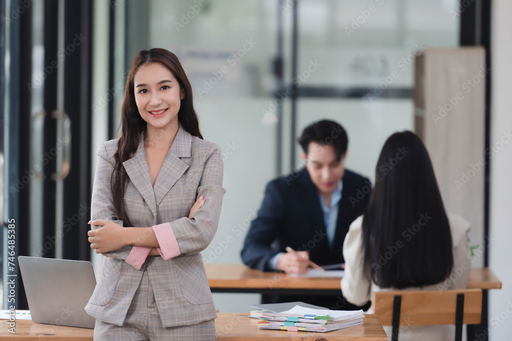 Fototapeta premium Portrait of beautiful businesswoman standing in the office room with her team in the background.