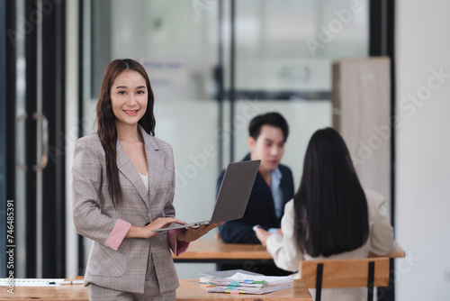 Professional businesswoman standing in the office room while holding laptop in her hands.