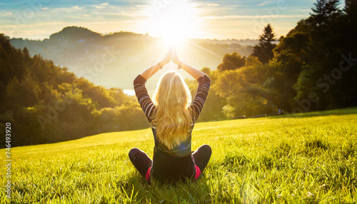 A young woman with long blond hair is meditating with her legs crossed and hands clasped above the head, sitting on a green meadow on a hill. Generative Ai.
