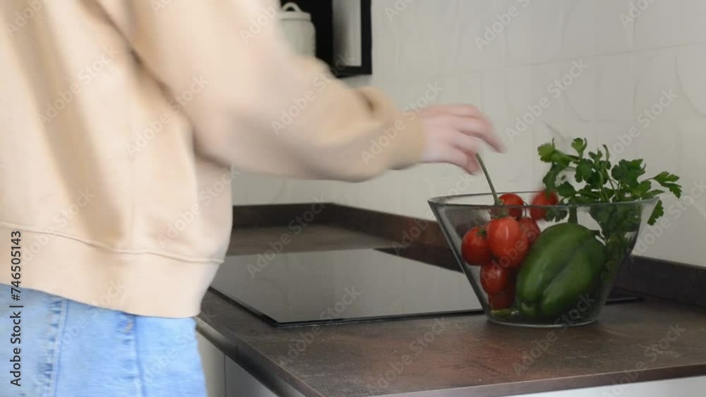 Female person in Casual Clothes Puting Vegetables to Transparent Bowl in the Kitchen in Minimalist Style. Nutrition and Healthy Lifestyle. Red Tomatoes, Green Pepper. Close-up of hands. Female person in Casual Clothes Puting Vegetables to Transparent Bowl in the Kitchen in Minimalist Style. Nutrition and Healthy Lifestyle. Red Tomatoes, Green Pepper. Close-up of hands.