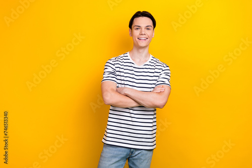 Photo of cheerful guy with stylish hairdo dressed striped t-shirt standing arms crossed isolated on vibrant yellow color background