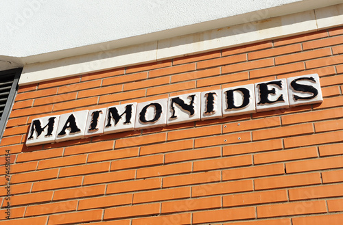 Maimonides. Rótulo de calle con azulejos típicos sevillanos con letras negras sobre fondo blanco en un muro de ladrillos rojos. Sevilla, España