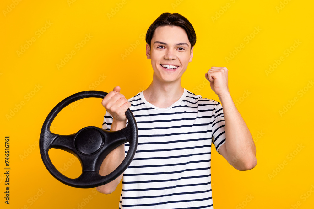 Photo of satisfied student dressed striped t-shirt holding steering wheel win vehicle in lottery isolated on vivid yellow color background Photo of satisfied student dressed striped t-shirt holding steering wheel win vehicle in lottery isolated on vivid yellow color background