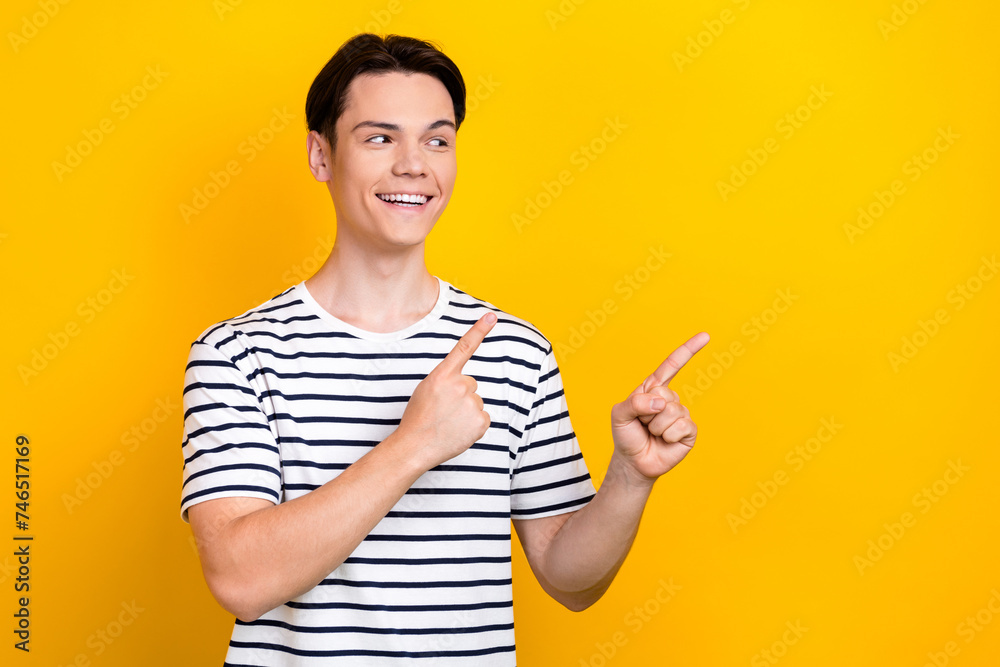 Photo of optimistic guy with stylish hairdo dressed striped t-shirt look directing at sale empty space isolated on yellow color background Photo of optimistic guy with stylish hairdo dressed striped t-shirt look directing at sale empty space isolated on yellow color background